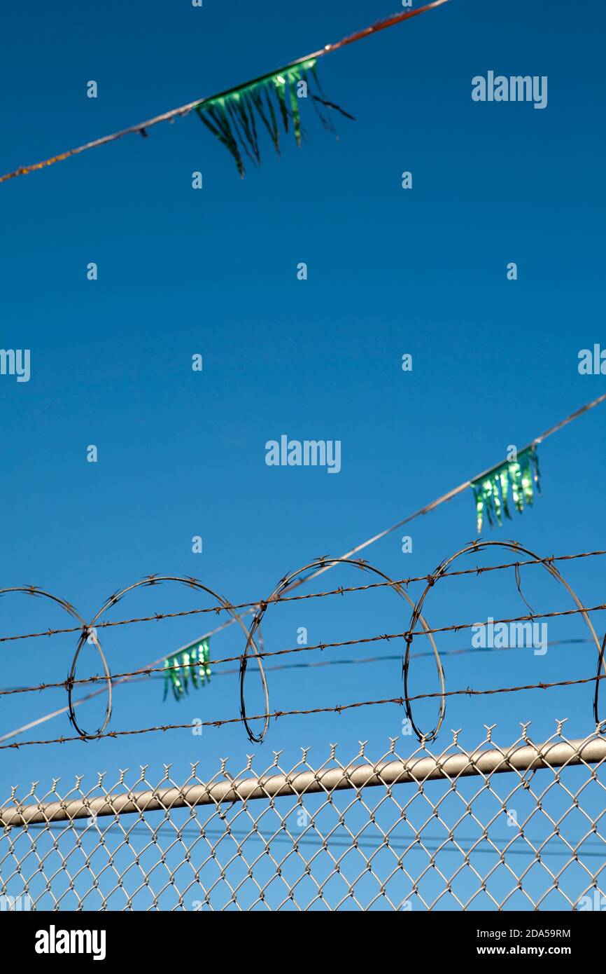 Metal fence,  barbed wire, razzor wire and glittery green streamers Stock Photo