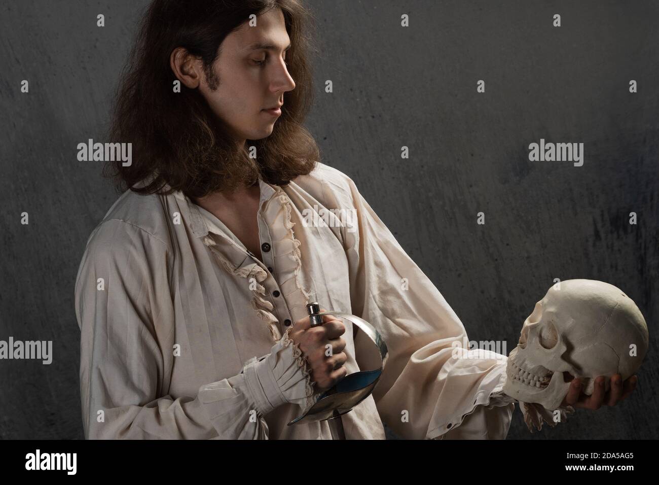 A romantic young man in a medieval costume with a sword says a Shakespearean monologue. The guy is holding a human skull. Stock Photo