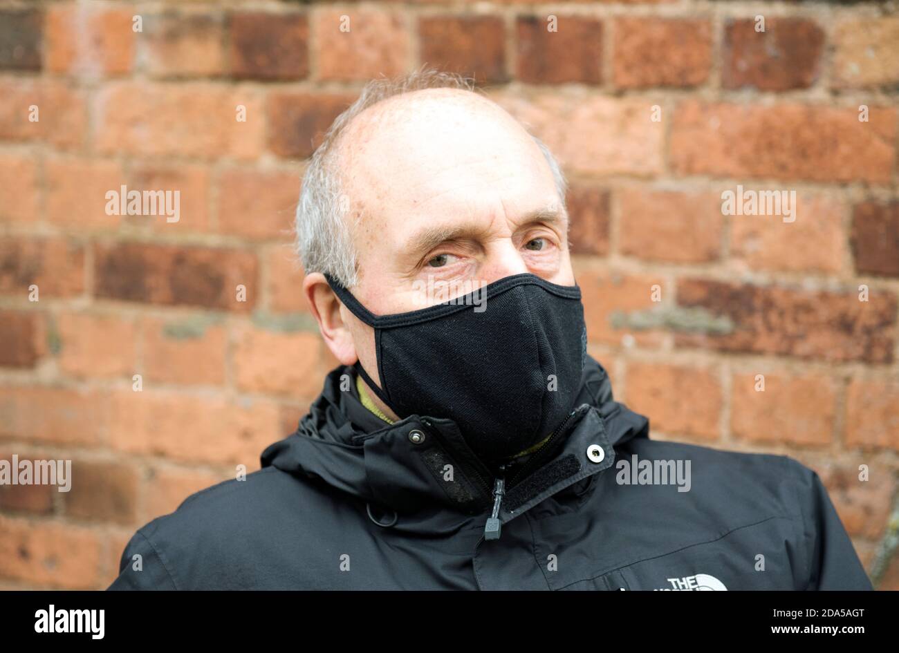 Close up of senior or elderly man wearing a black mask or face covering and black anorak outside. Stock Photo