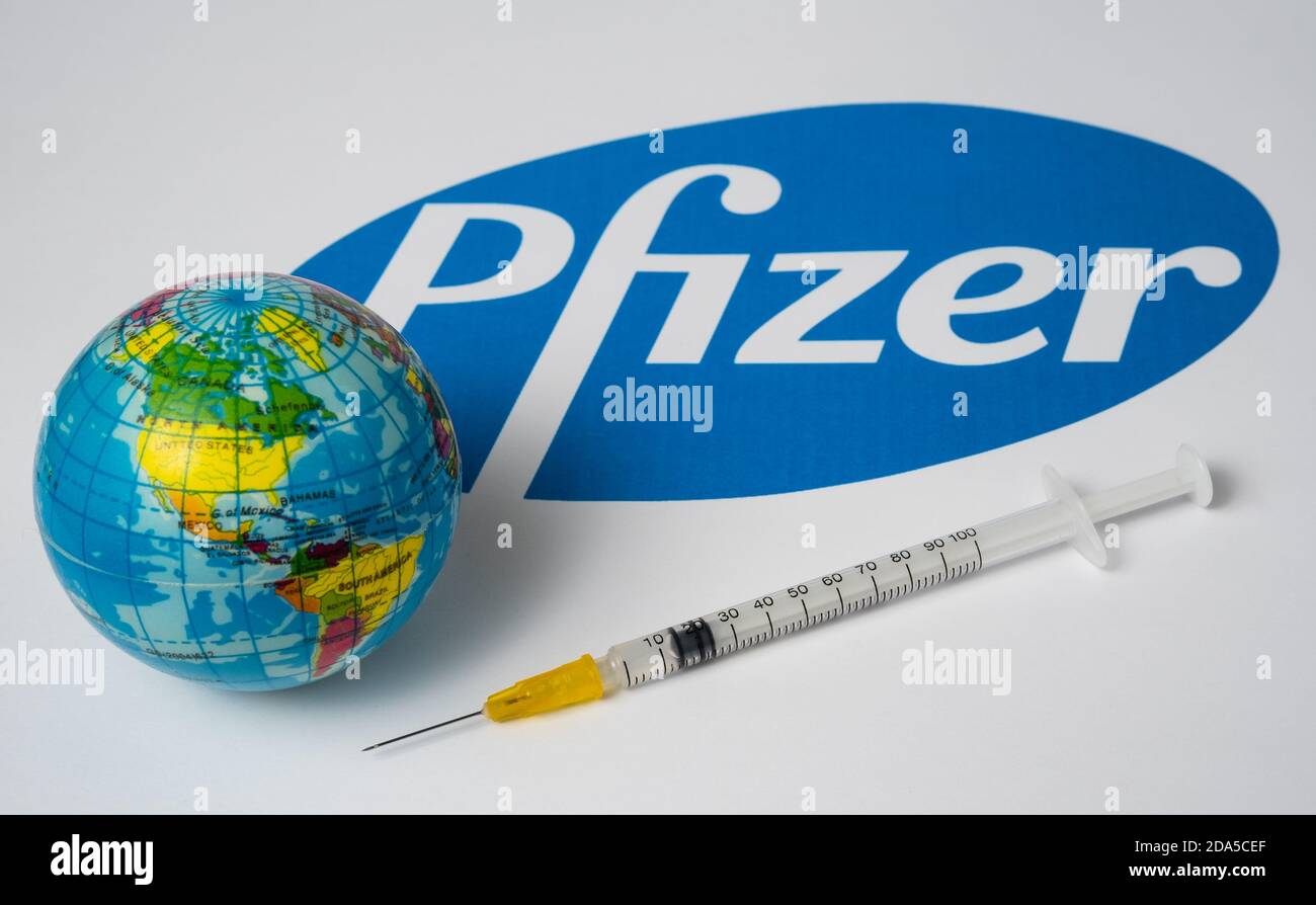 Stafford / United Kingdom - November 9 2020: Pfizer Covid-19 vaccine concept. Syringe and a blurred toy globe with blurred Pfizer company logo on the Stock Photo