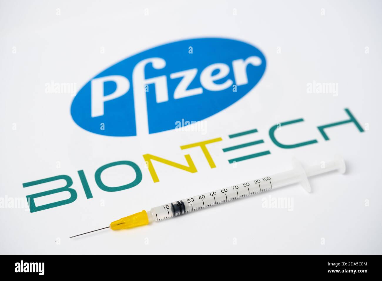 Stafford / United Kingdom - November 9 2020: Pfizer BioNTech Covid-19 vaccine concept. Syringe balanced on a fingertip and blurred company logos on th Stock Photo