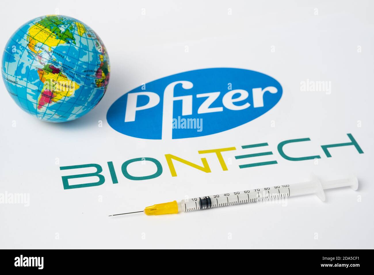 Stafford / United Kingdom - November 9 2020: Pfizer BioNTech Covid-19 vaccine concept. Syringe and a blurred toy globe with blurred company logos on t Stock Photo