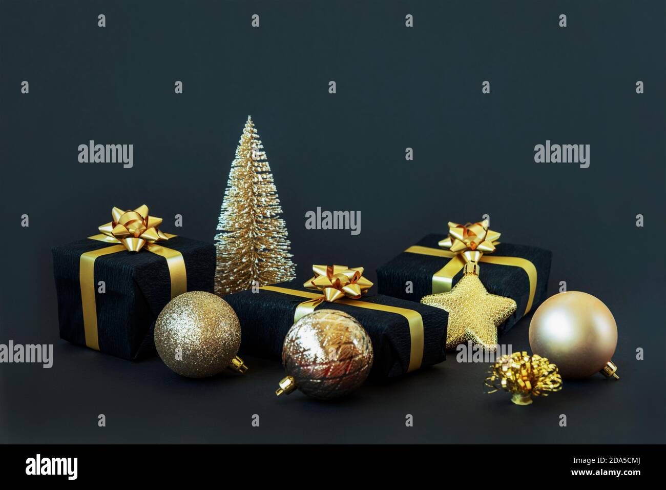 Black gift boxes with golden ribbon, balls and toy Christmas tree on ...