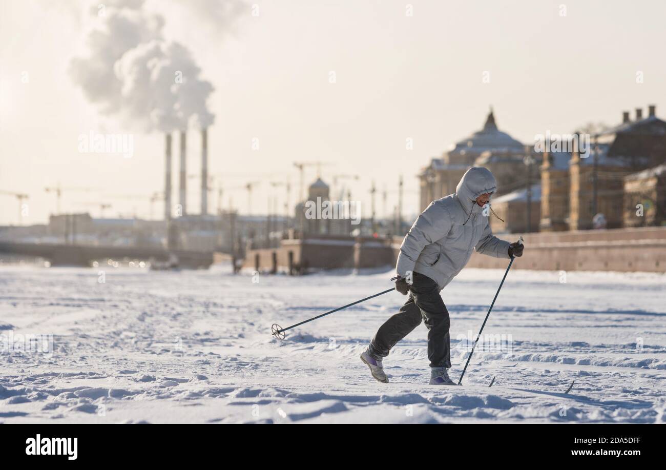 Woman skier riding on ice of the frozen Neva River at sunny day, winter in St.Petersburg, bridge on background Stock Photo