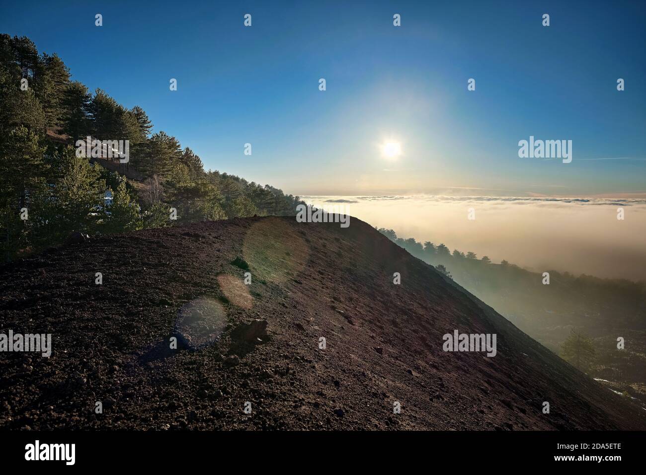 volcanic ashes of Mezza Luna crater and low clouds at sunset in Etna Park, Sicily (lens flare) Stock Photo