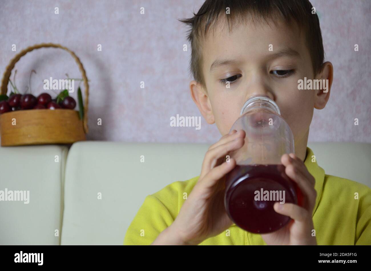 Cute little boy drinking juice at home, cherry juice drinks from a
