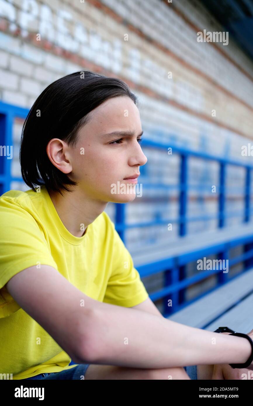 Side view portrait of a pensive thoughtful teen boy. teenager sitting on stadium stairs. thinking of problem or reflecting, anxious melancholic guy serious face feel lonely or doubtful and worried. Stock Photo