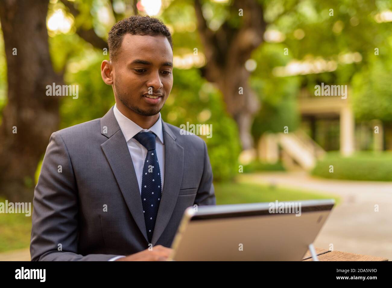 African businessman sitting outdoors using laptop computer while ...