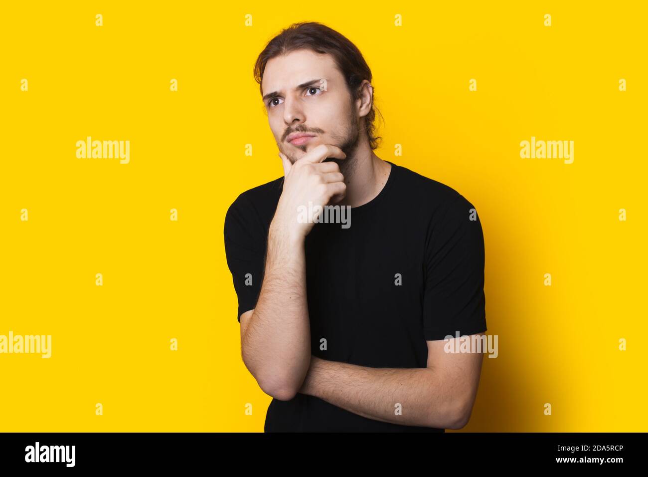Pensive caucasian man in black shirt is touching his chin thinking ...