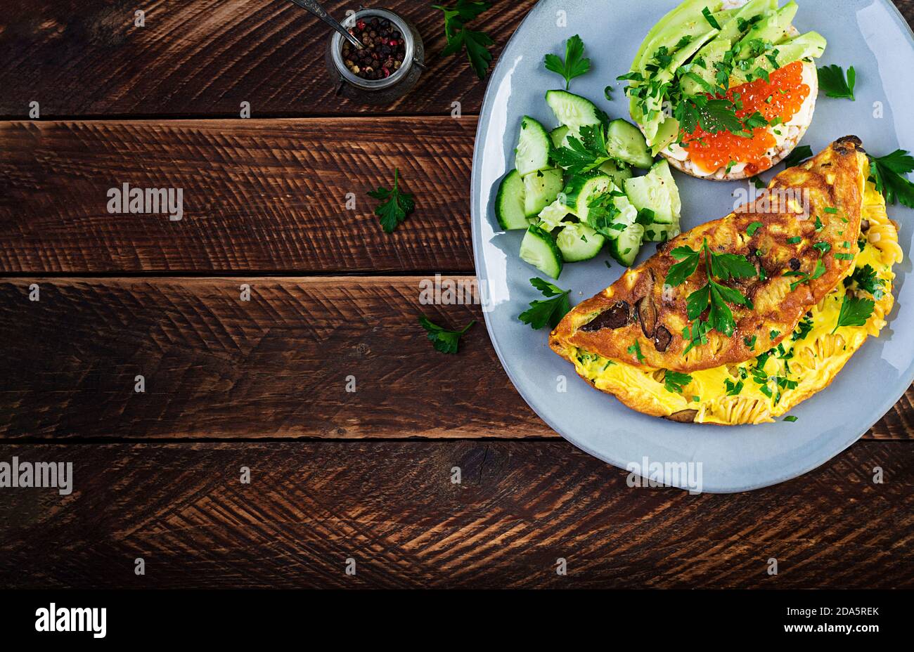 Omelette with forest mushroom, fusilli pasta and sandwich wich red caviar, avocado on plate.  Frittata - italian omelet. Top view, overhead, copy spac Stock Photo