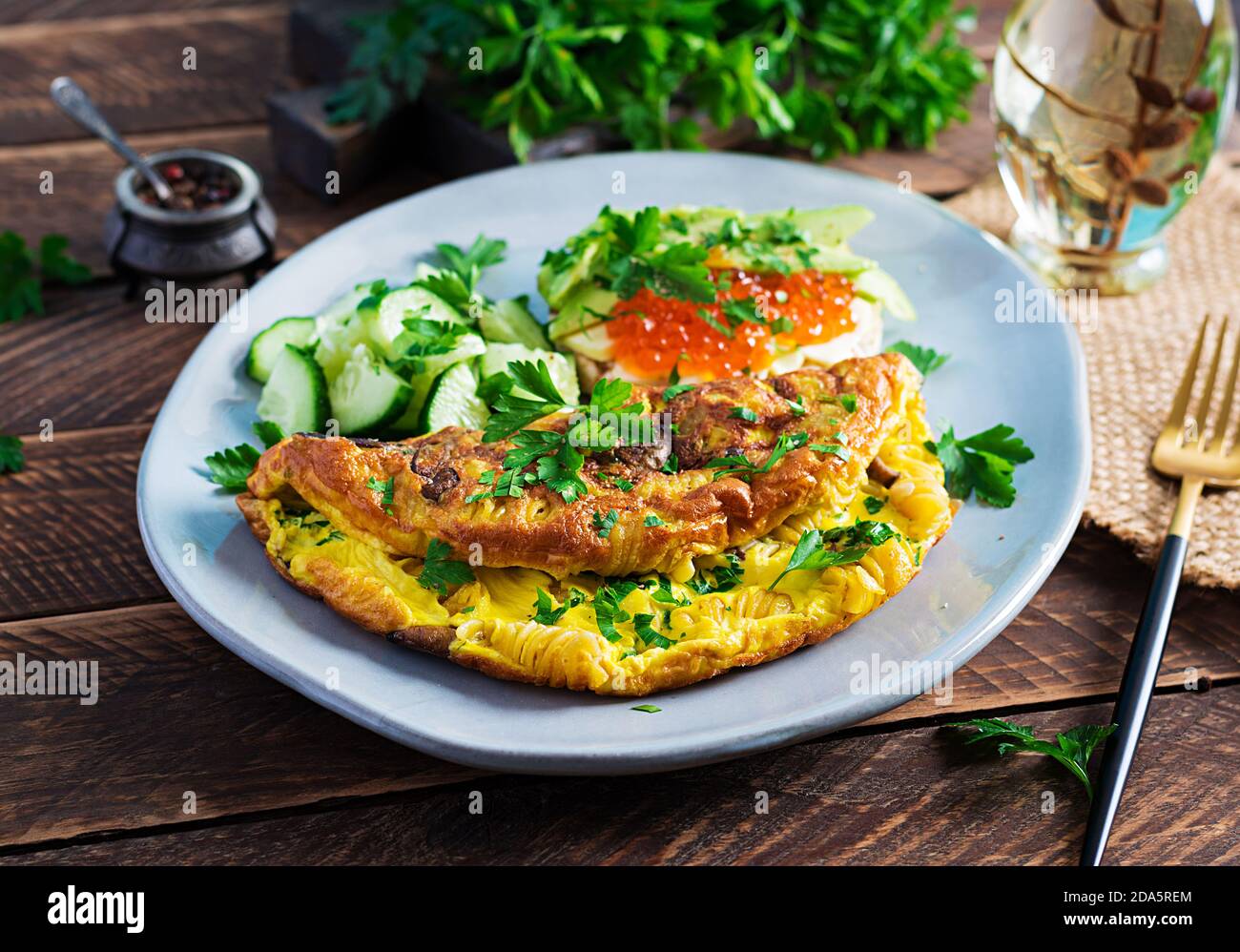 Omelette with forest mushroom, fusilli pasta and sandwich wich red caviar, avocado on plate.  Frittata - italian omelet. Stock Photo