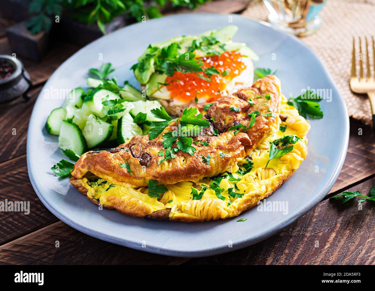 Omelette with forest mushroom, fusilli pasta and sandwich wich red caviar, avocado on plate.  Frittata - italian omelet. Stock Photo