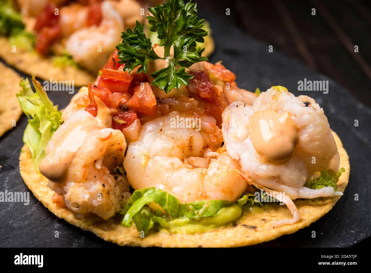 shrimp tacos on hard shell tortilla with Mexican garnish on dark wood