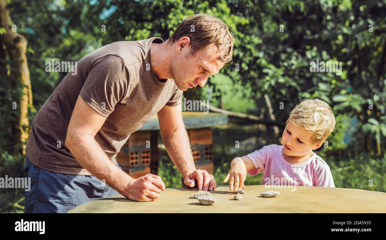 Father son play outside sun day, show explain driving traffic regulation rules use stone imitation cars. Instruction hand palm finger gesture Stock Photo