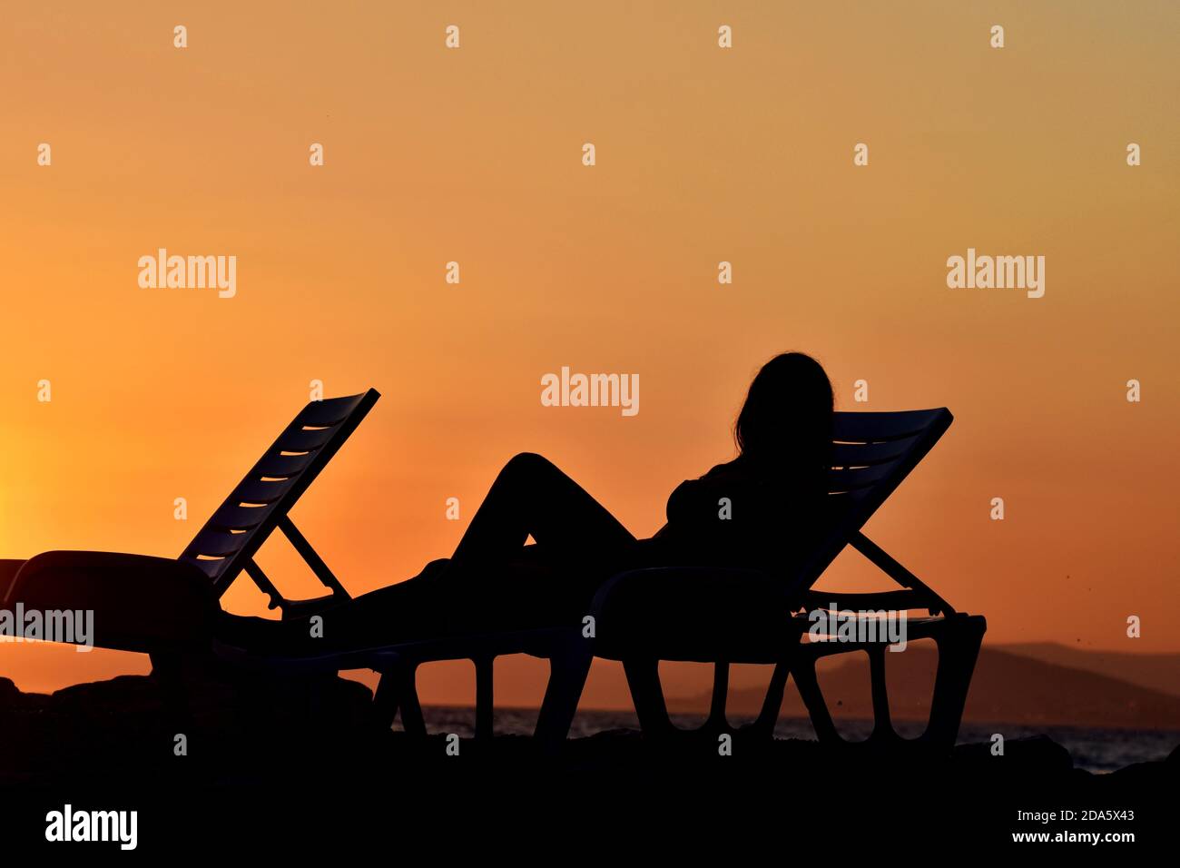 Beautiful silhouette of a woman in a chair on the beach on a sunset ...