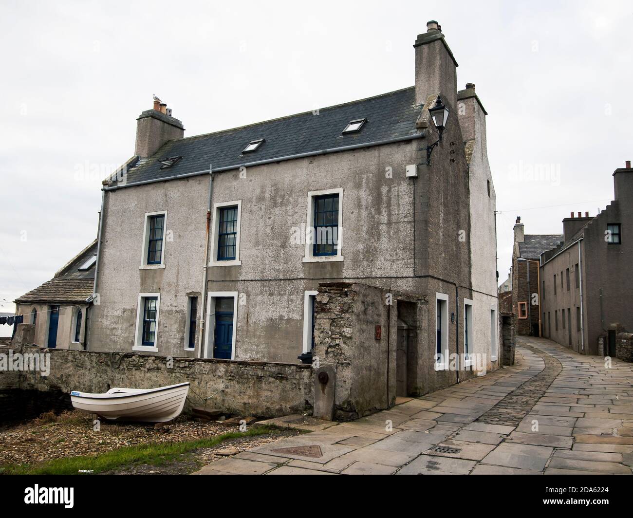 Big grey building on narrow pebble street bend in Stromness on Orkney Stock Photo