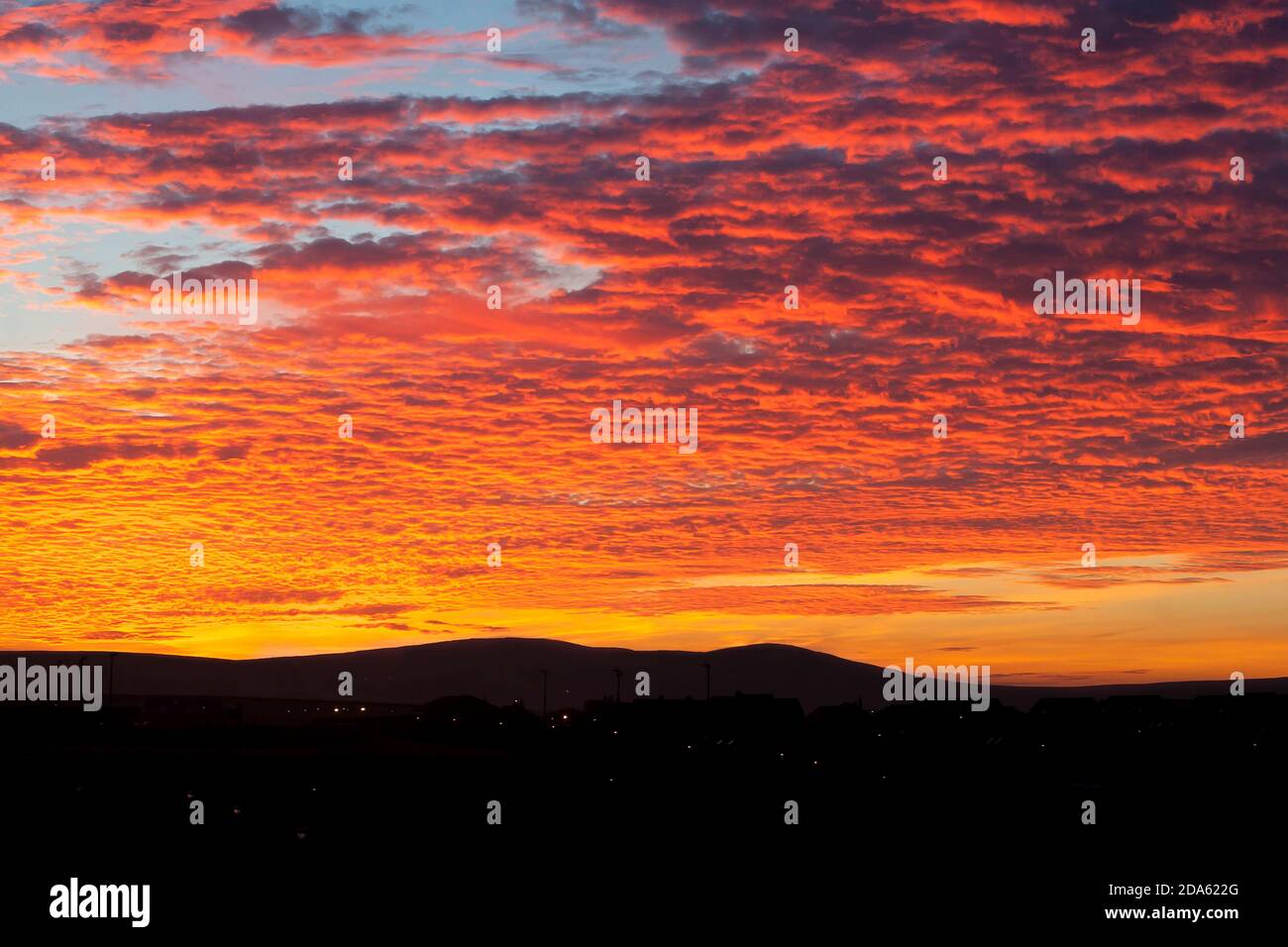 Multicolor sunrise clouds above black buildings and hills in scottish town Stromness on Orkney islands Stock Photo