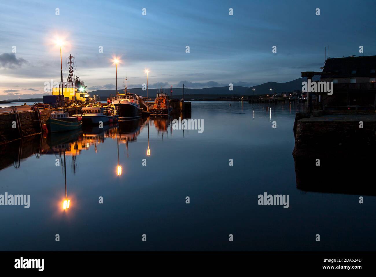 Stromness harbour with boats and lights before sunrise and blue sky reflections on water Stock Photo