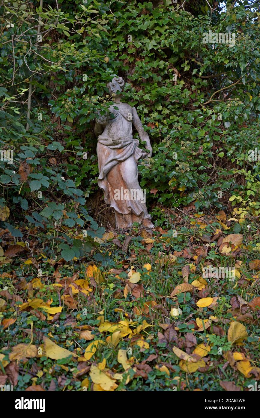 A classical greek stone statue of a woman surrounded by autumn leaves