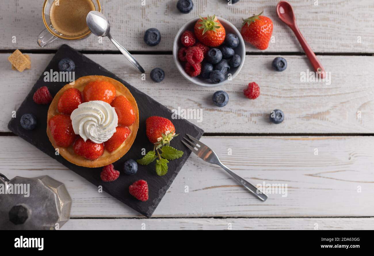 Homemade organic strawberry pie with raspberry and blue berry with a coffee on a white wooden table.Top view. Stock Photo
