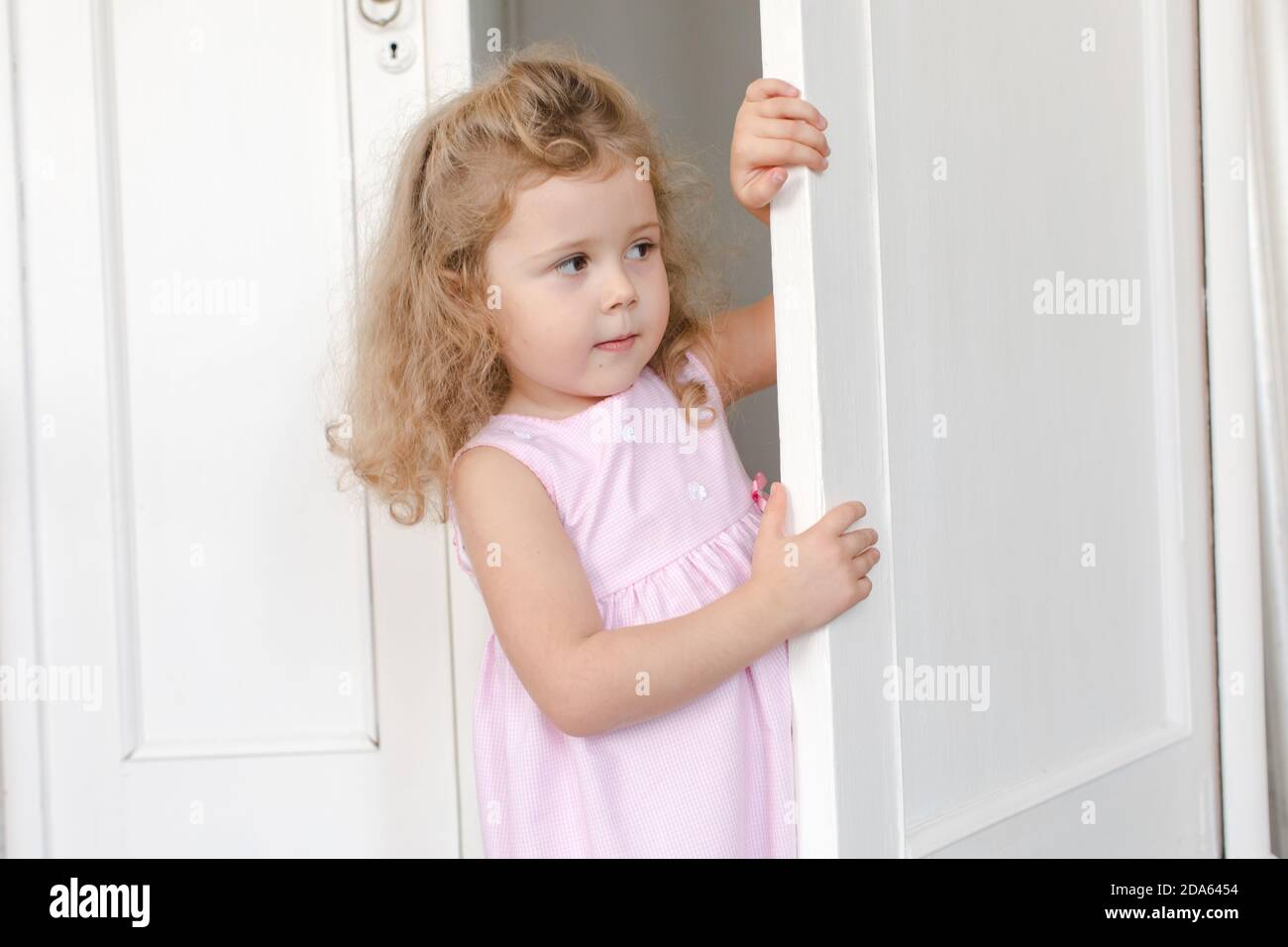 Cute girl peeping out of door in room Stock Photo