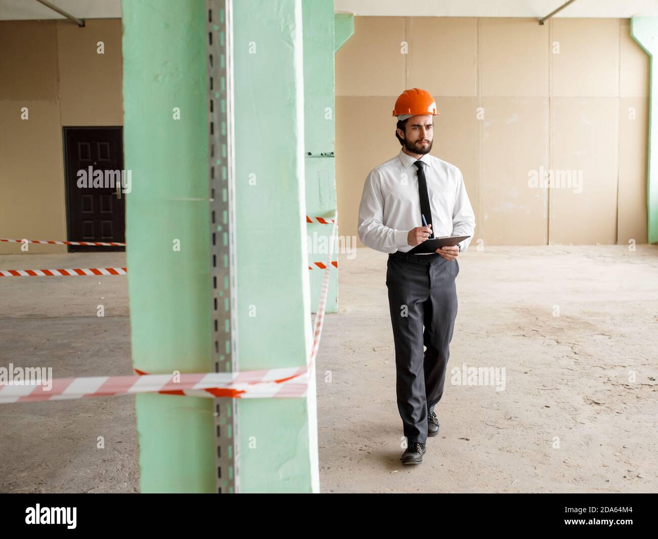 A young bearded Architect in a construction helmet on a construction site checks the result Stock Photo