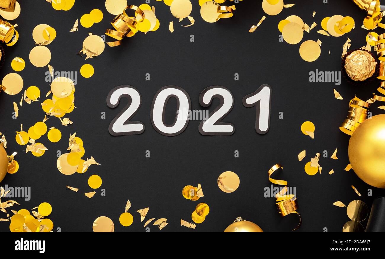 2021 white text lettering in golden confetti, Christmas festive decor frame on black background. Happy New year event composition Stock Photo