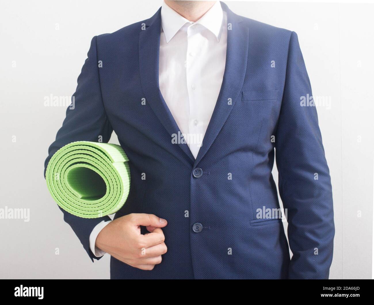 A young business man in a suit and jacket stands and holds a exercise and yoga mat close at hand. The concept of work and rest of office employees. Wo Stock Photo