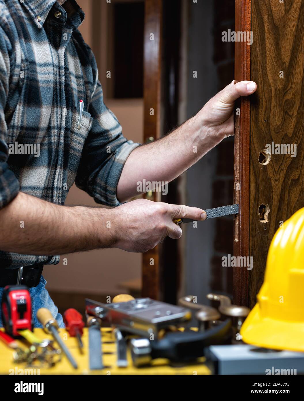 Close-up. Carpenter with the rasp prepares the hole for the lock of a wooden door. Construction industry. Stock Photo