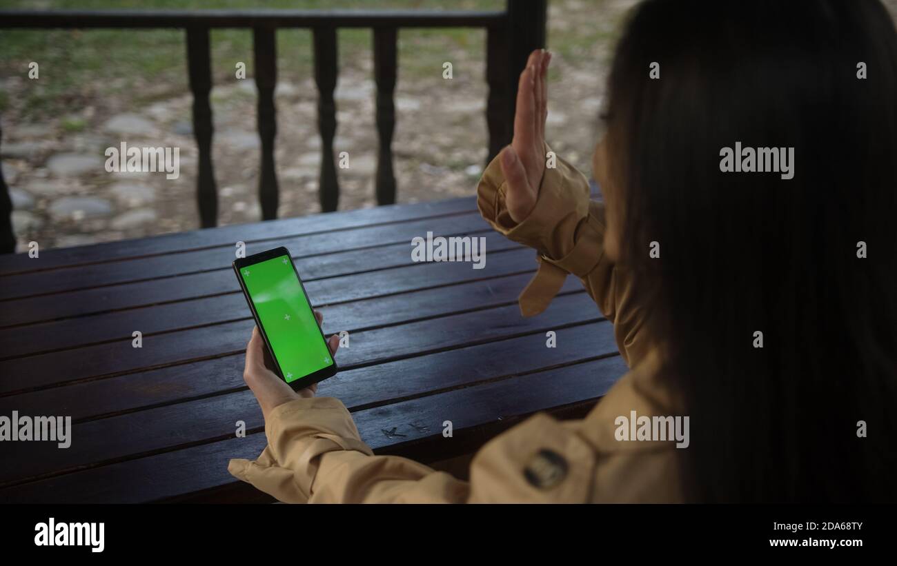 Young woman at nature sitting on a bench using with Green Mock-up Screen Smartphone in Horizontal Landscape Mode. Girl Using Mobile Phone, Browsing In Stock Photo