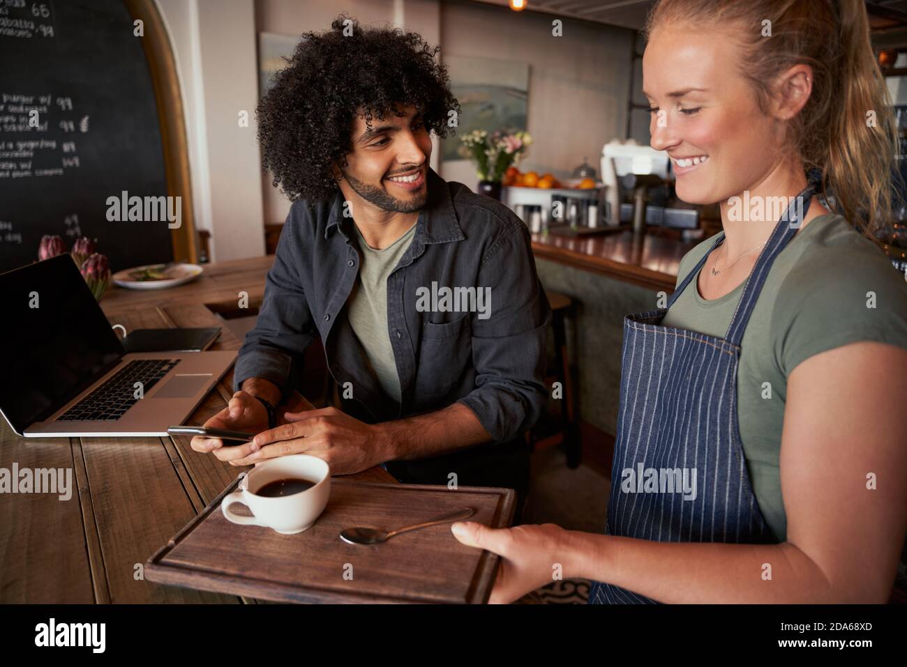 Beautiful young waitress serving man with curly hair with coffee on table Stock Photo