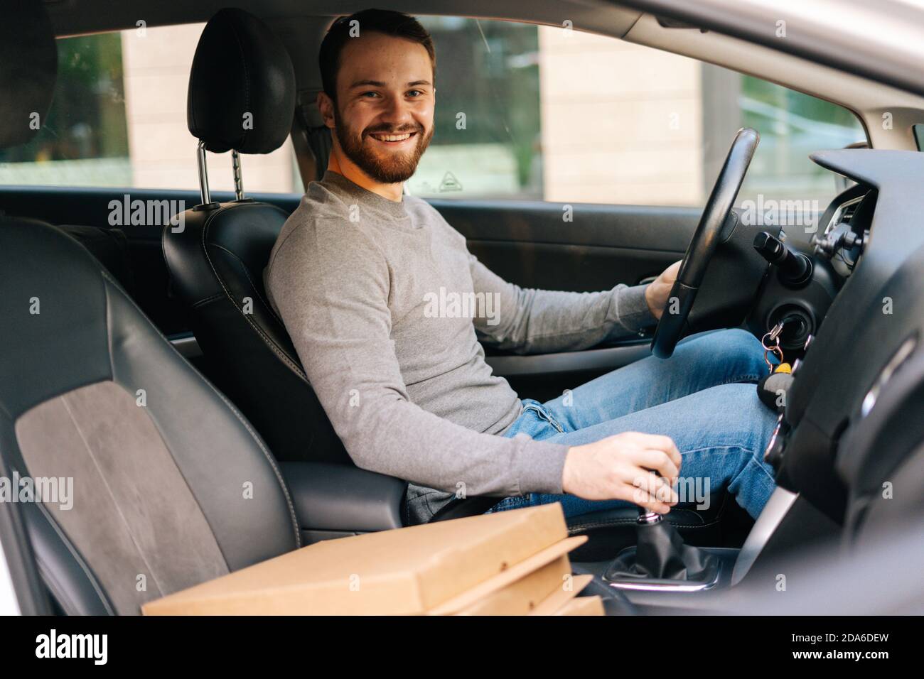Cheerful delivery man wearing casual clothes driving car delivered hot