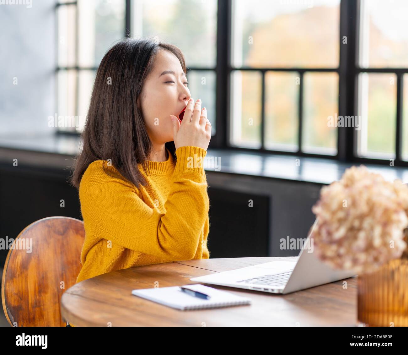Asian woman yawning due to overworking and exhausting. Young lady in bright yellow jumper Stock Photo