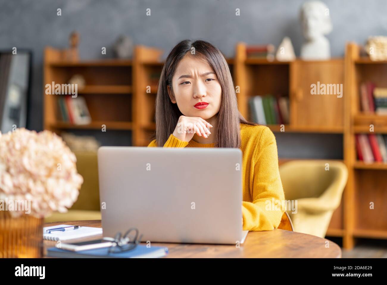 Unhappy frowning asian woman forgetting smth working on laptop Stock Photo