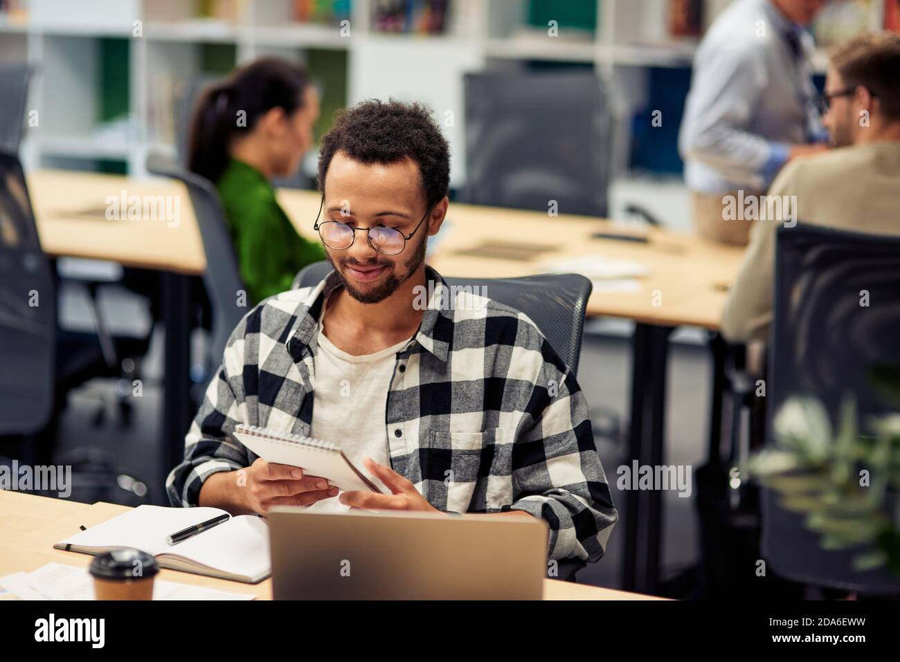 Young happy mixed race man reading notes while working in the modern office, selective focus. Business and startup concept Stock Photo