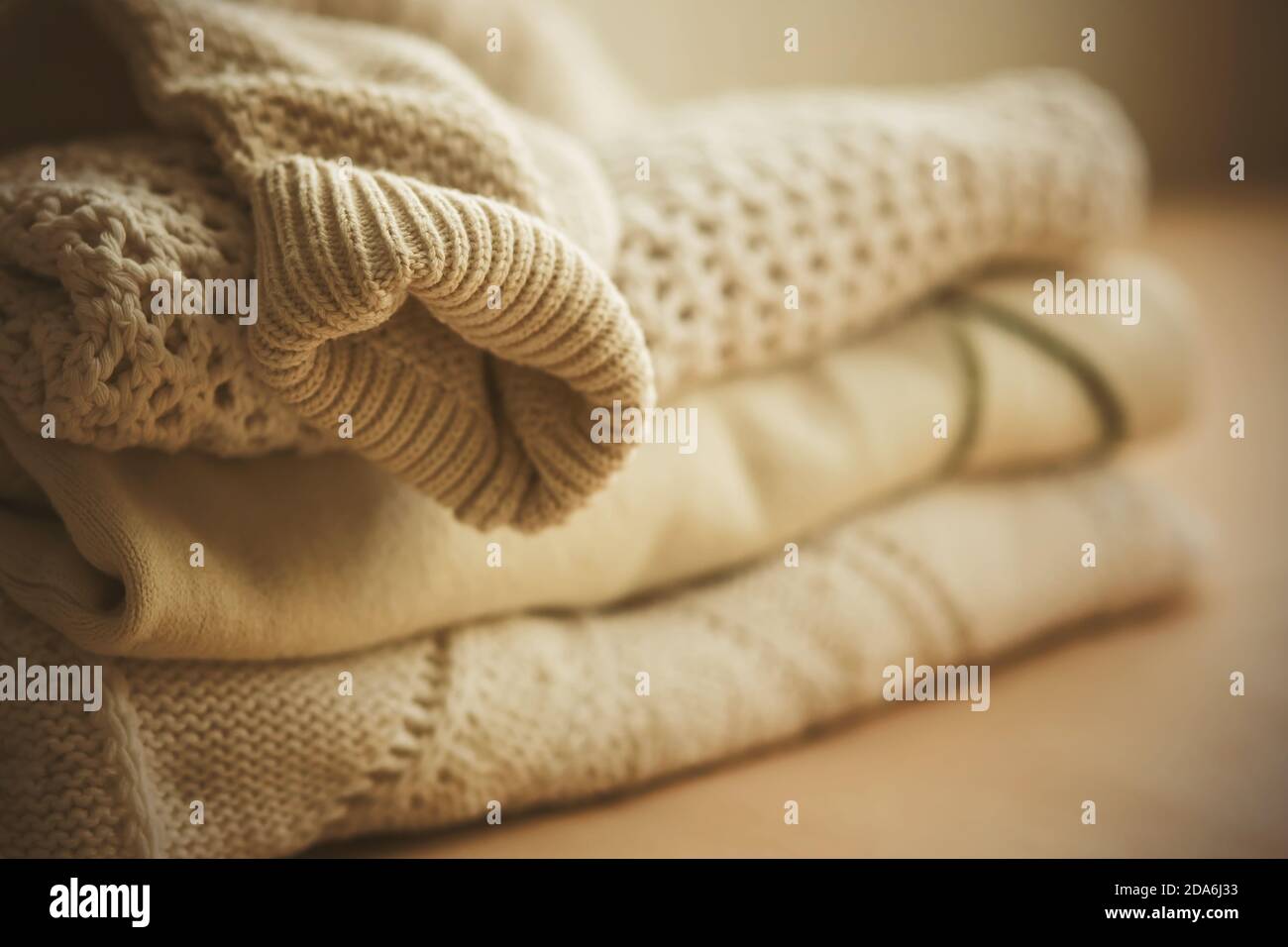 A neat stack of white warm wool sweaters, with the sleeve of one of them hanging down from the top, illuminated by the light. Clothing for cold weathe Stock Photo