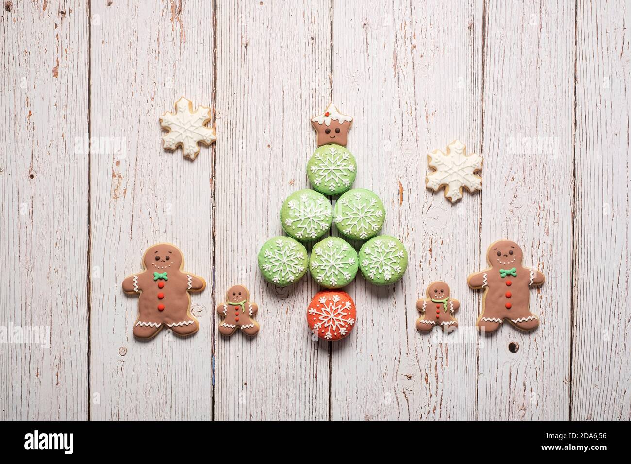 Christmas tree made of decorated macarons macaroons with gingerbread man cookie family standing next to it on a wood background with copy space Stock Photo