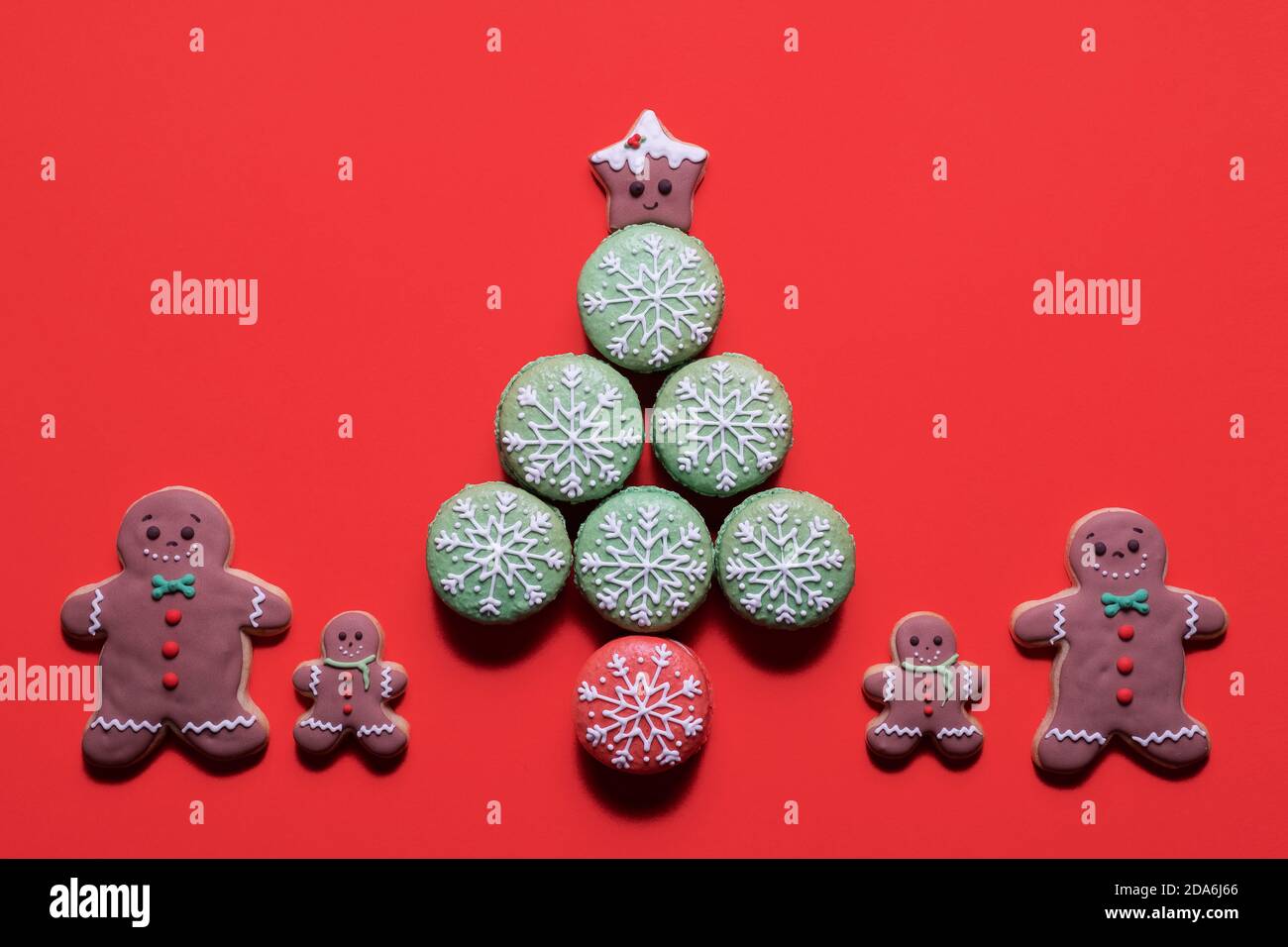 Christmas tree made of decorated macarons macaroons with gingerbread man cookie family standing next to it on a red background with copy space Stock Photo