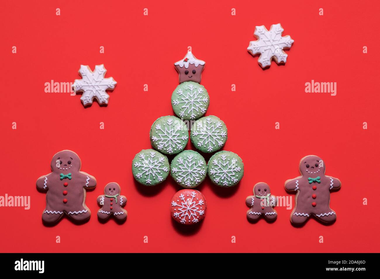 Christmas tree made of decorated macarons macaroons with gingerbread man cookie family standing next to it on a red background with copy space Stock Photo
