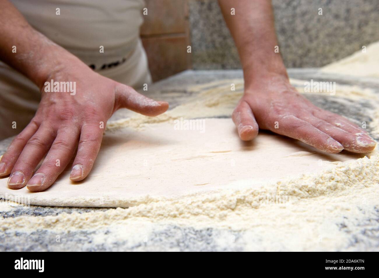 the pizza maker spreads the leavened bread dough with his hands before