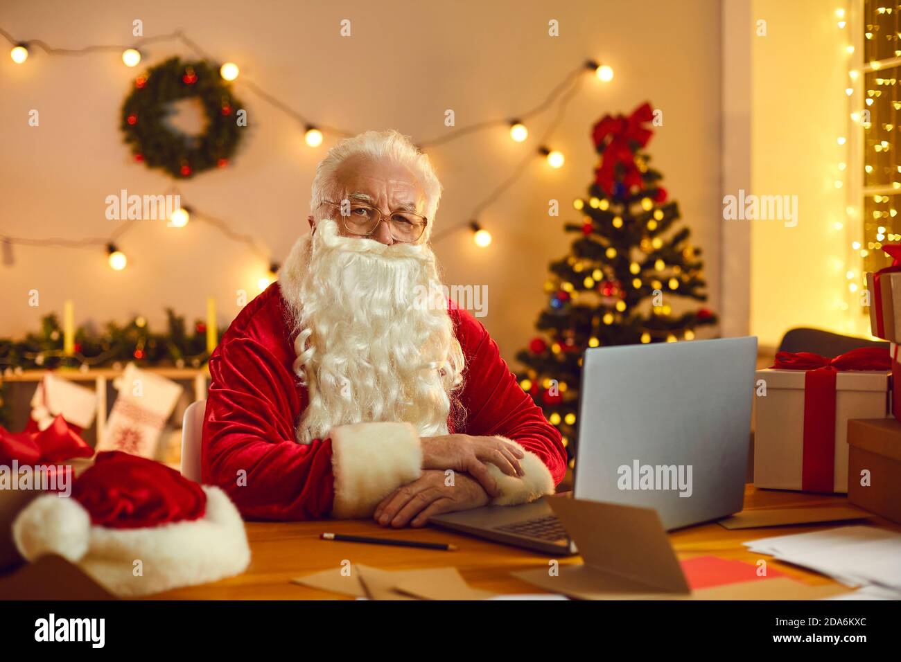 Mature Santa in traditional red costume ready to congratulate online at home Stock Photo