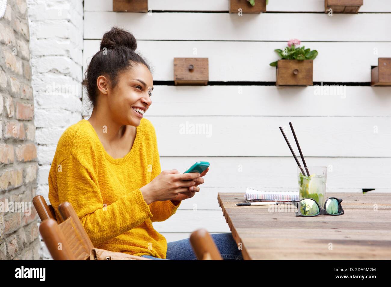 Side view portrait of cheerful young african woman sitting at cafe with ...