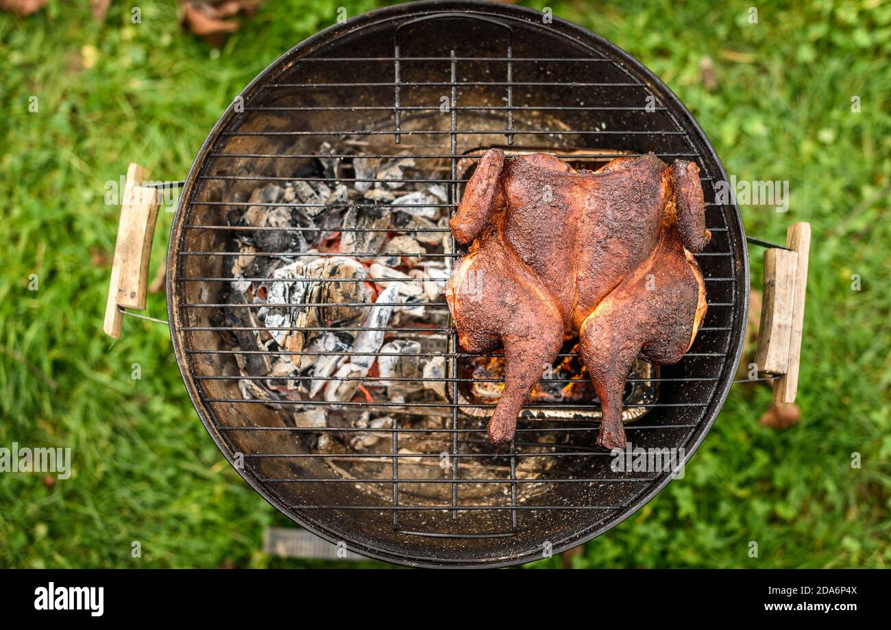 Traditional spatchcocked barbecue chicken al mattone on charcoal grill. Grilling and smoking spatchcock chicken outdoors on firewood BBQ grill in natu Stock Photo