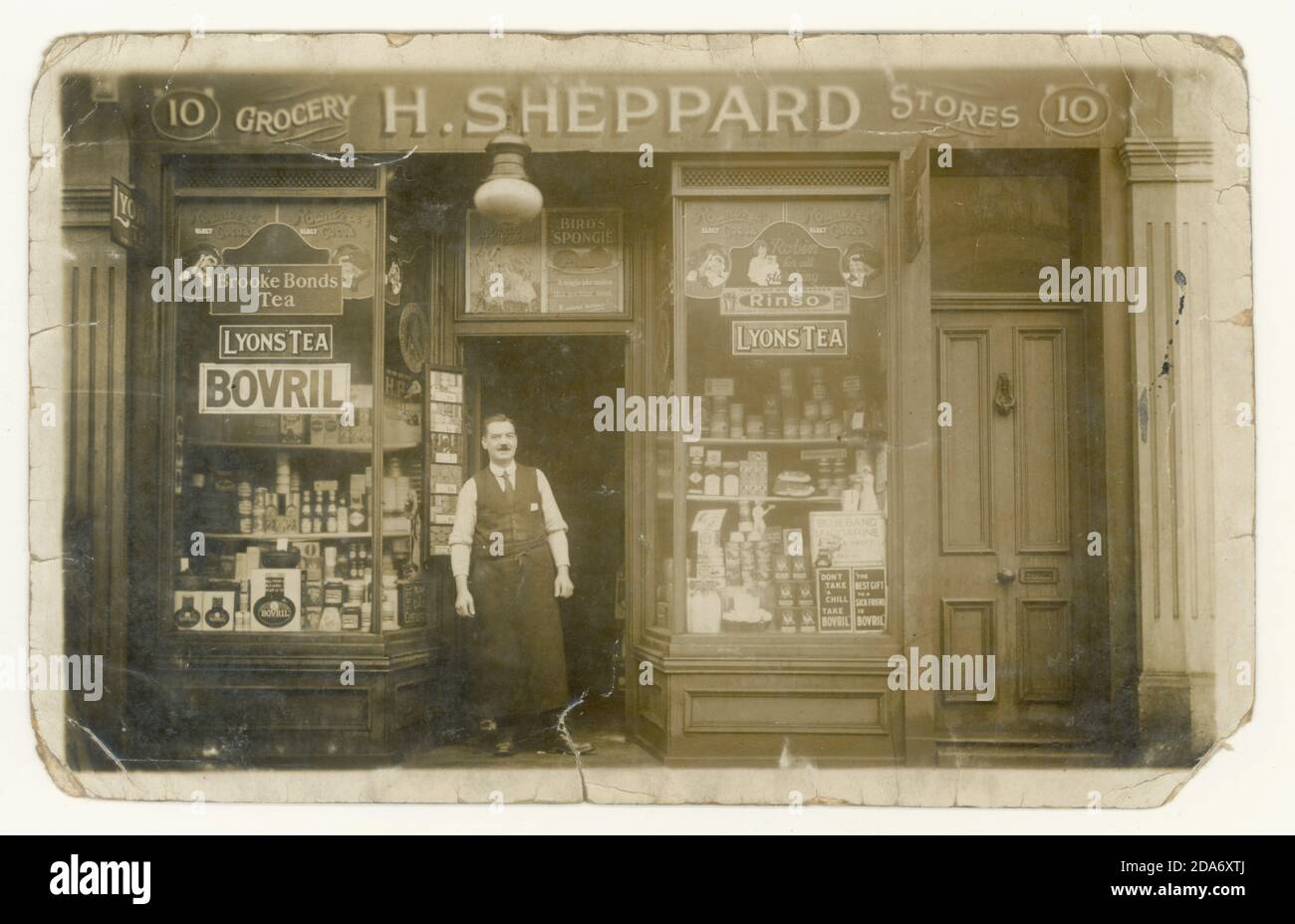 Original WW1 era postcard of Grocery store with many well known brand names in the shop window display adverts:   Rowntree's, Rinso, Lyons Tea, Brooke Bonds Tea, Bovril, Bird's Spongie (cake mix)  Blue Band Margarine, HP Sauce, and Quaker Oats -  The proprietor is  H. Sheppard, circa 1917, 1918,  Erdington, Birmingham, England, U.K. Stock Photo