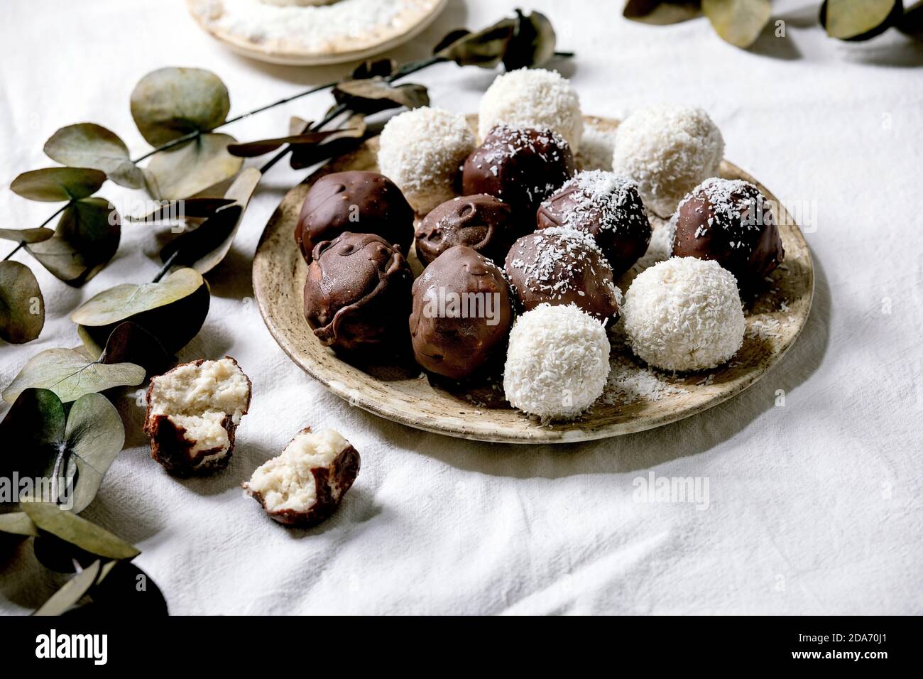 Raw vegan coconut chocolate candy balls over white with eucalyptus