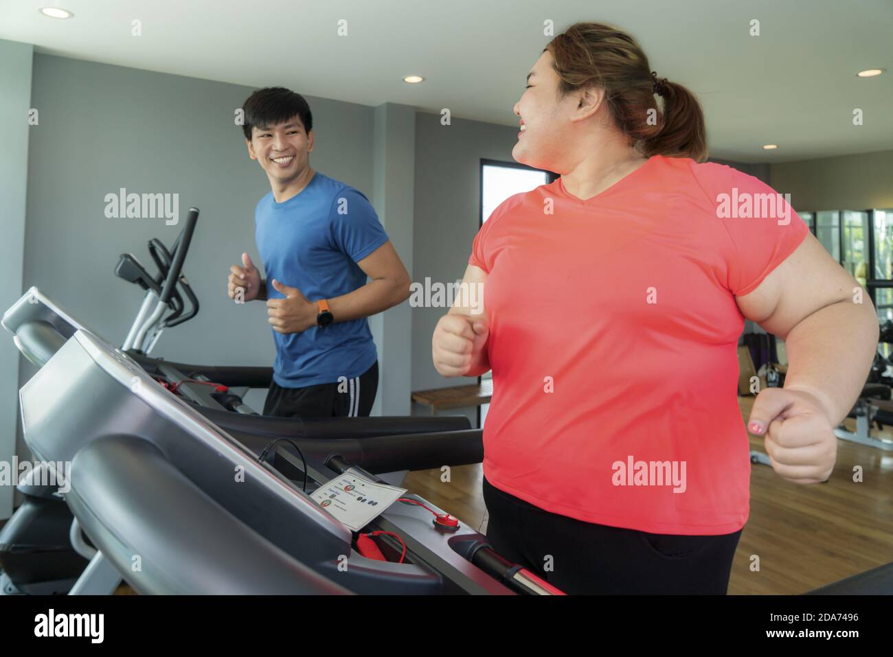 Two Asian trainer man and Overweight woman exercising training on treadmill in gym, trainer thump up to her for good result during workout. Fat women Stock Photo