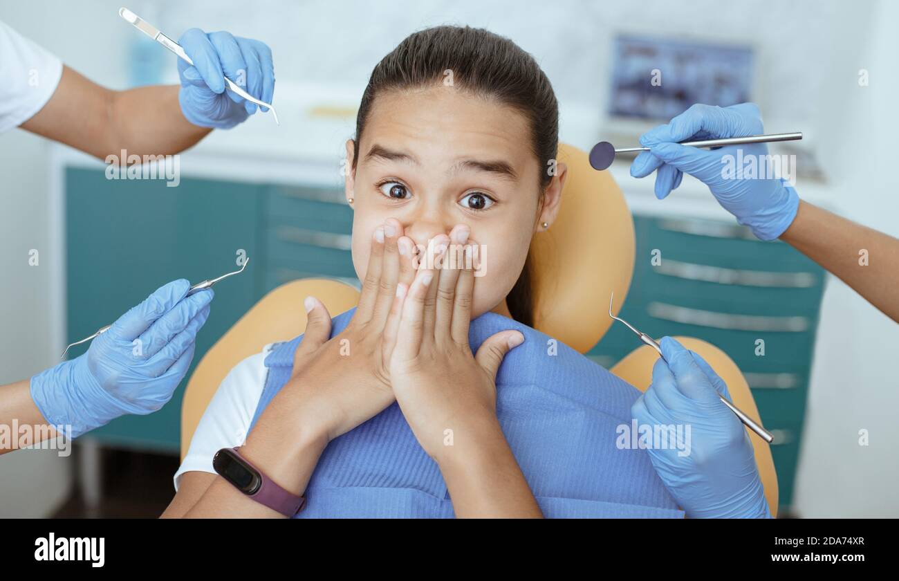 Shocked little girl with wide open eyes closed her mouth and does not give doctors to treat teeth Stock Photo