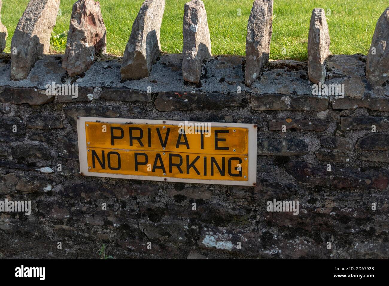 a close up view of a private no parking sign that has been attached on a stone wall outside a private residence Stock Photo