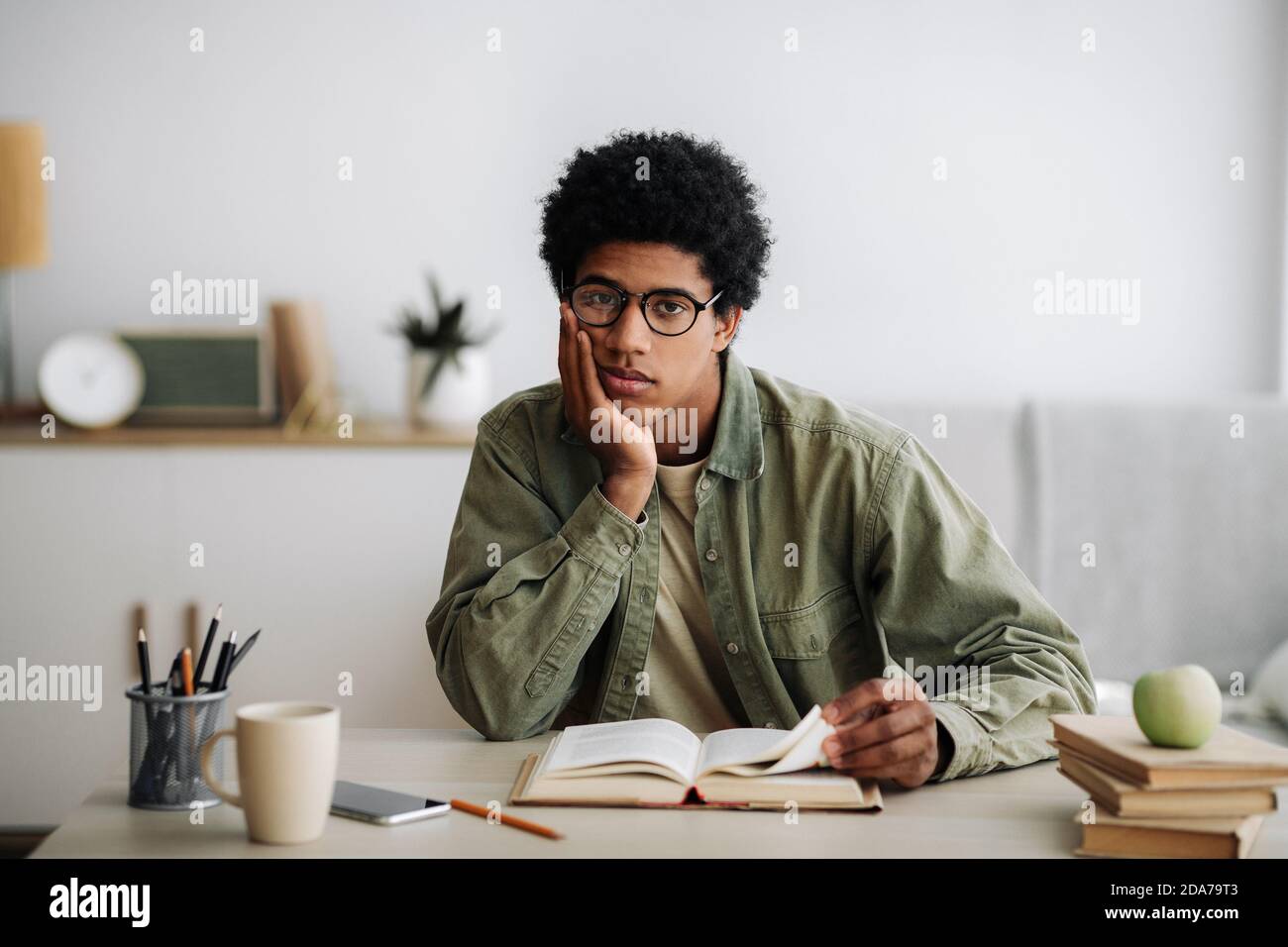 Distance education concept. Bored African American student with textbook studying at home Stock Photo