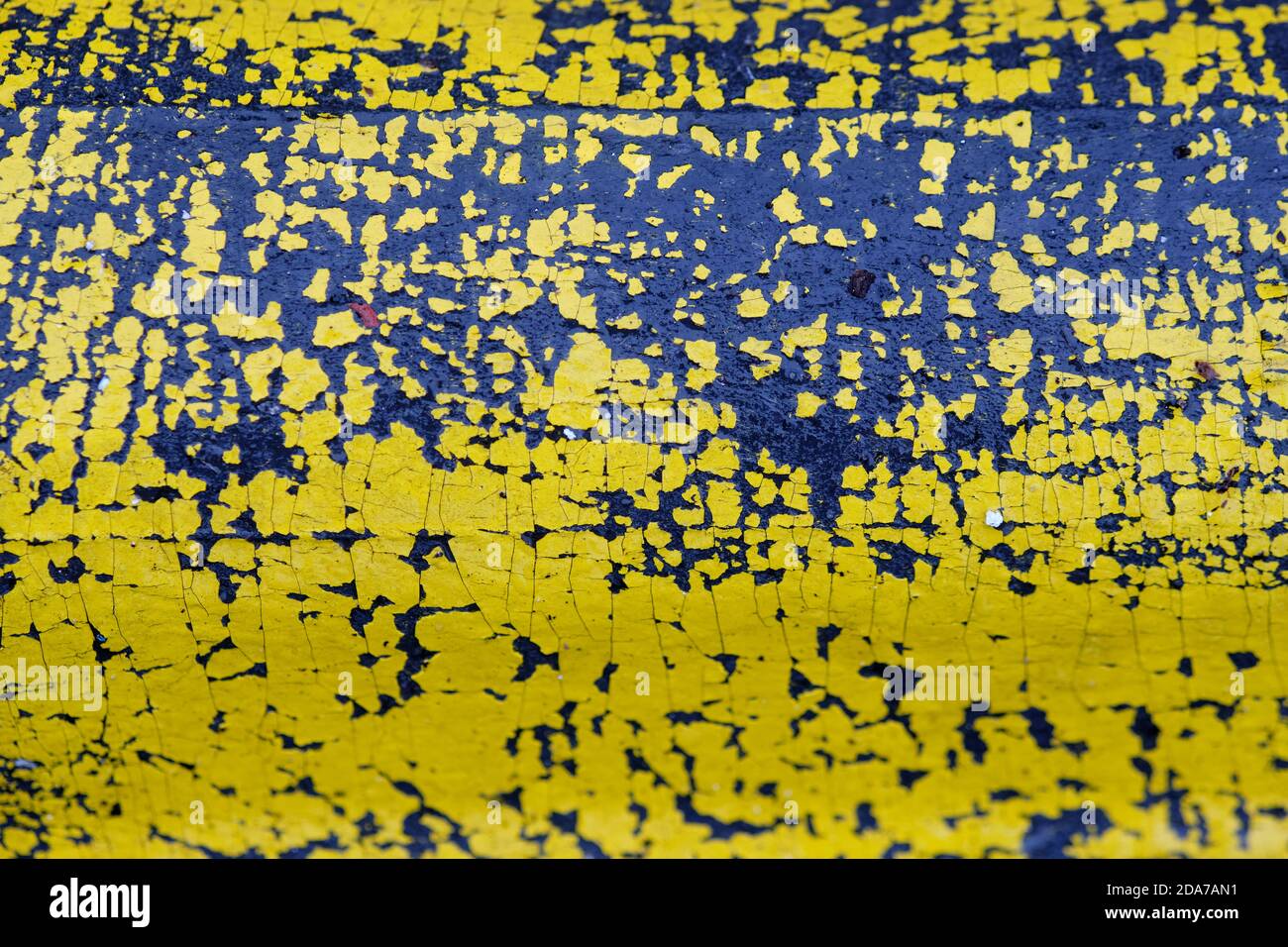 Background with close-up of yellow paint flaking off a black wet plastic part of a road boundary. Seen in Germany in October. Stock Photo